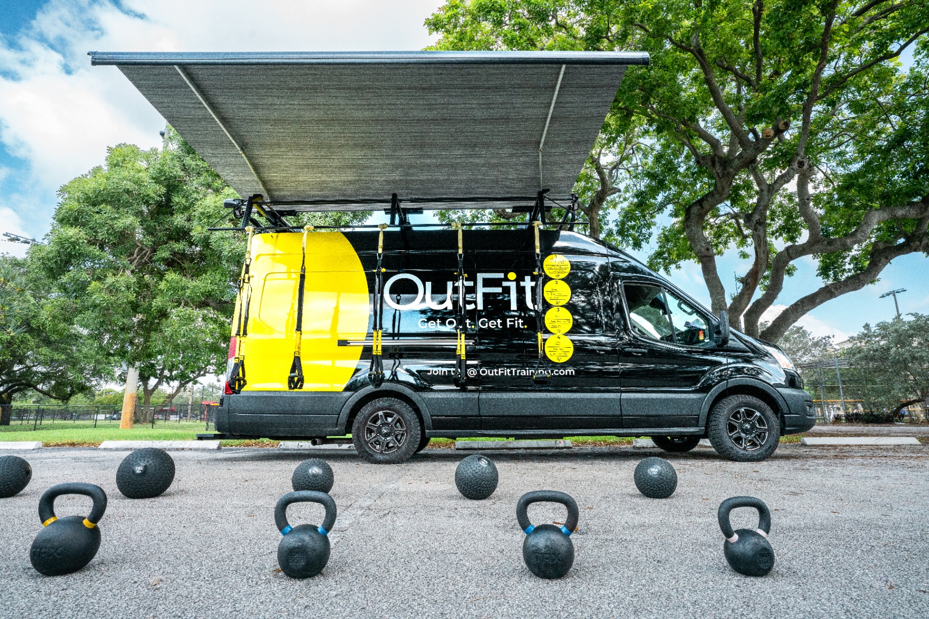 The yellow OutFit Training van parked at a Plantation park with TRX straps set up for class
